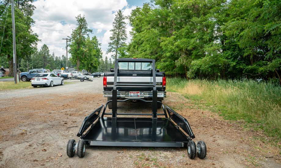 A TUFFLIFT deck lowered flat to the ground behind a truck on a gravel road